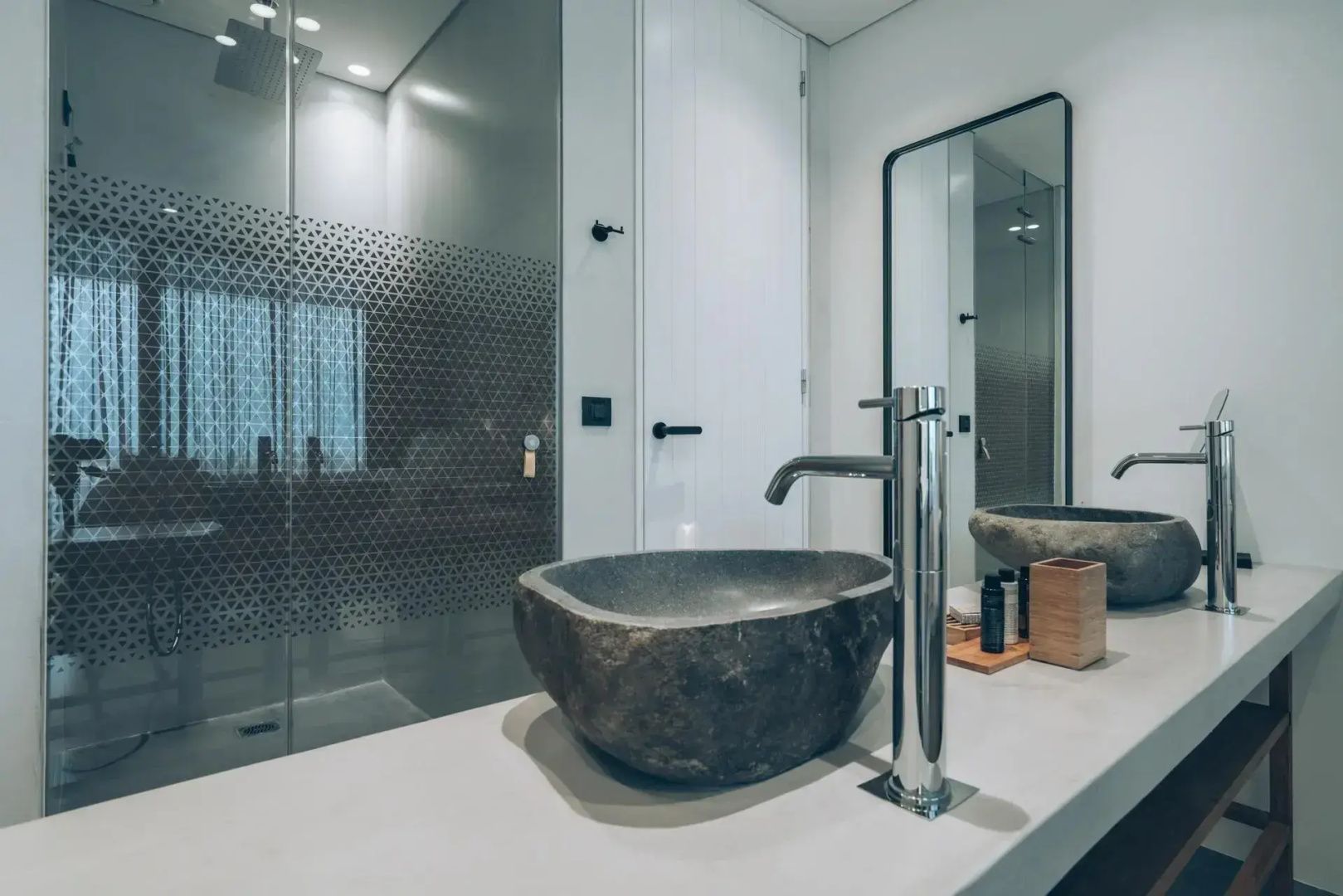 Waschtisch im Badezimmer mit Steinwaschbecken, moderner Armatur und gläserner Duschkabine.