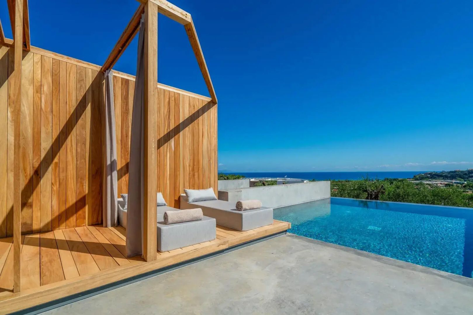 Holzpavillon mit zwei Sonnenliegen auf einer Terrasse direkt neben einem Infinity-Pool mit Meerblick.