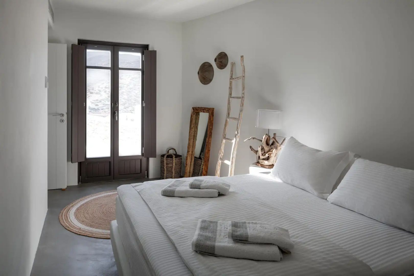 Schlafzimmer mit Doppelbett, Holzleiter als Dekoration, Standspiegel und Zugang zur Terrasse.