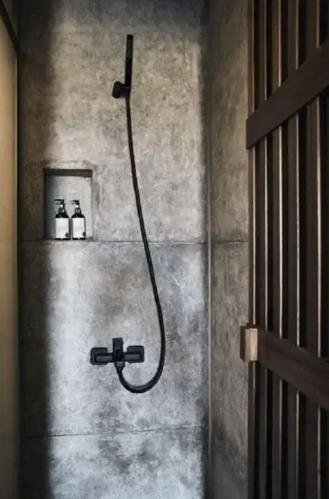 Badezimmer mit grauer Wand in Betonoptik, schwarzer Duscharmatur und Wandnische.