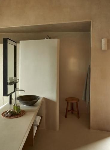 Badezimmer in Erdtönen mit einem Naturstein-Waschbecken, Spiegel und Holzhocker.