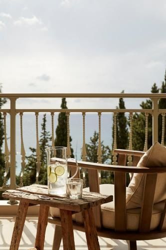 Terrasse mit Geländer, Holzstühlen und einem Tisch mit einer Karaffe Wasser vor Meerblick.
