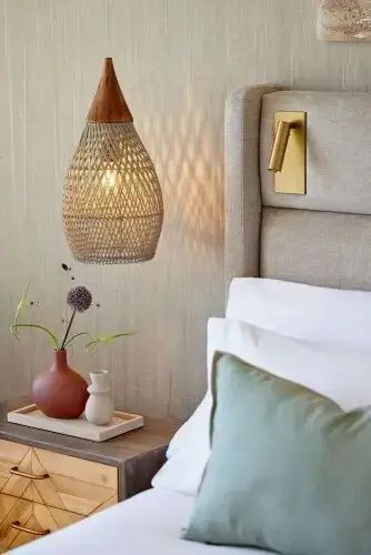 Nahaufnahme einer geflochtenen Hängelampe neben dem Bett und einer kleinen Vase auf dem Nachttisch.