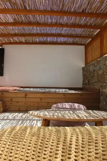 Überdachte Terrasse mit Holzmöbeln, Sitzkissen und einer Natursteinwand im Sonnenschein.