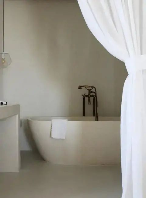 Freistehende weiße Badewanne mit eleganter dunkler Armatur und weißem Vorhang im Badezimmer.