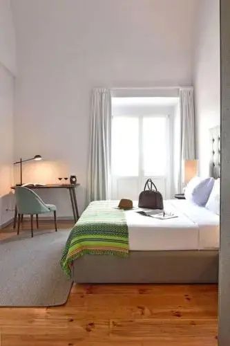 Modernes Hotelzimmer mit einem Doppelbett, grünem Überwurf und einem Schreibtisch am Fenster.