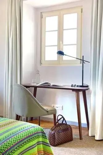 Schreibtisch aus Holz mit Stuhl und Lampe vor einem hellen Fenster.