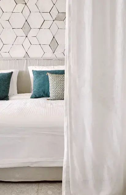 Bett mit weißen Kissen und blauen Akzentkissen vor einer Wand mit Sechseckfliesen.