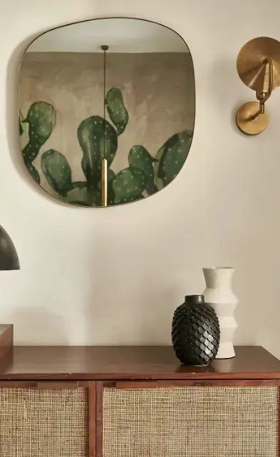 Wanddekoration mit Kaktusmotiv, Wandleuchte und zwei Keramikvasen auf einem Holzmöbel.