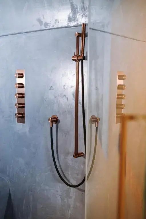 Moderne Dusche mit kupferfarbenen Armaturen und Handbrause an grauer Betonwand.