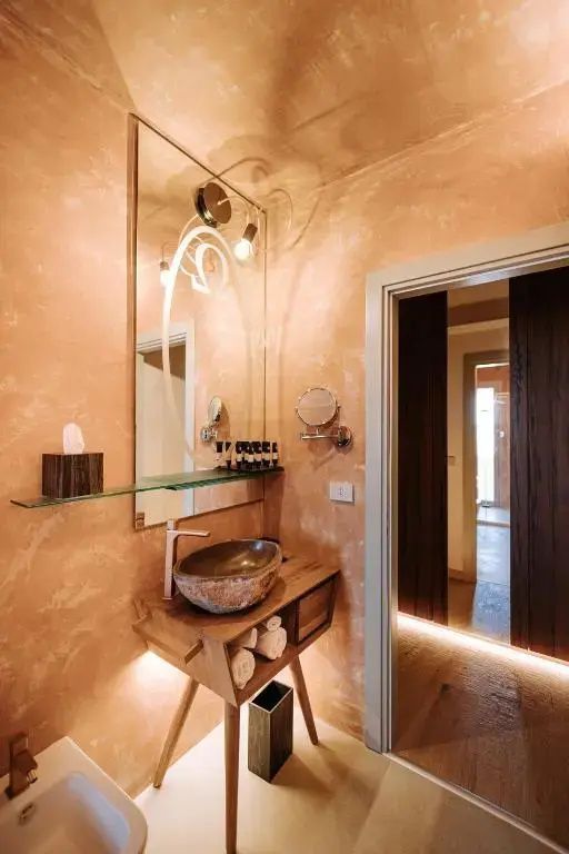 Badezimmer mit Steinwaschbecken auf einem Holzwaschtisch und beleuchtetem Spiegel.