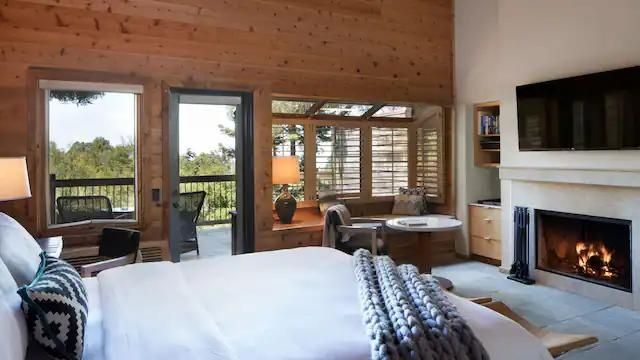 Hotelzimmer mit Holzverkleidung, Bett im Vordergrund, Sitznische am Fenster und Balkontür.