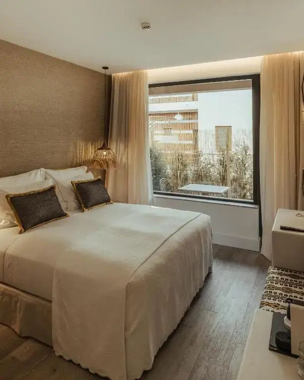 Doppelbett im modern eingerichteten Zimmer mit Fensterausblick auf den Außenbereich.