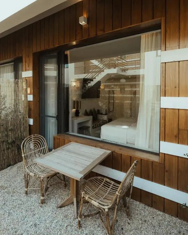 Außenbereich mit Holzverkleidung, zwei Rattan-Stühlen und einem Tisch auf Kieselsteinboden.