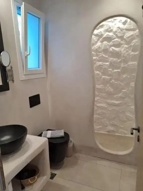 Badezimmer mit schwarzem Aufsatzwaschbecken, Toilette und Dusche mit Steinwand.