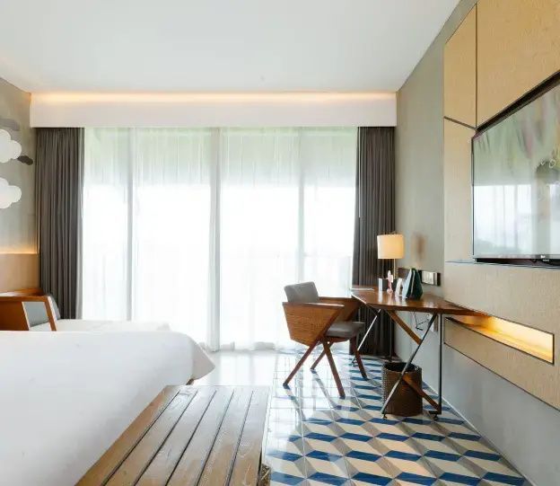Schreibtisch, Fliesenboden und große Fensterfront in einem hellen Hotelzimmer.