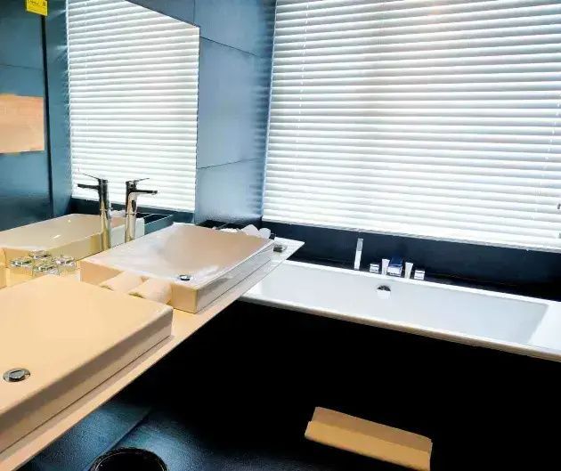 Badezimmer mit weißem Waschbecken, großer Spiegelwand und einer Badewanne am Fenster.