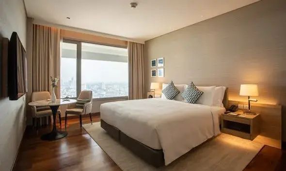 Hotelzimmer mit großem Doppelbett und großflächiger Fensterfront mit Blick auf die Stadt.