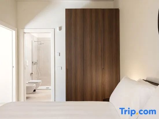 Hotelzimmer mit weiß bezogenem Bett, hohem Holzschrank und Blick ins angrenzende Badezimmer.