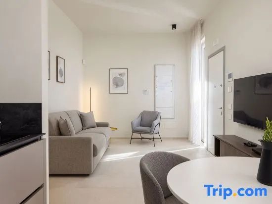 Heller Wohnbereich mit grauem Sofa, Sessel, weißem Esstisch und großen Fenstern.