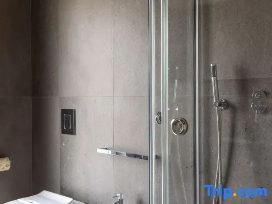 Badezimmer mit grauen Wandfliesen, gläserner Duschkabine und Handbrause.