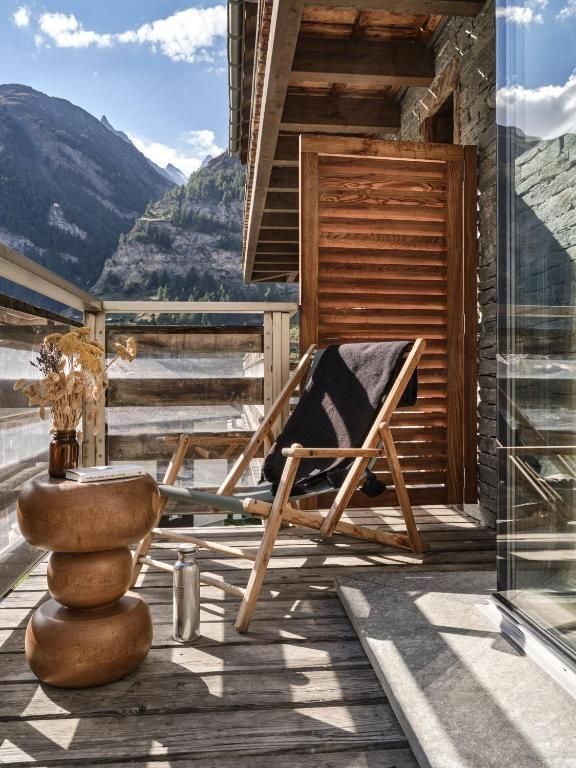 Balkon mit Holzliegestuhl und Beistelltisch mit Blick auf die umliegende Bergwelt.