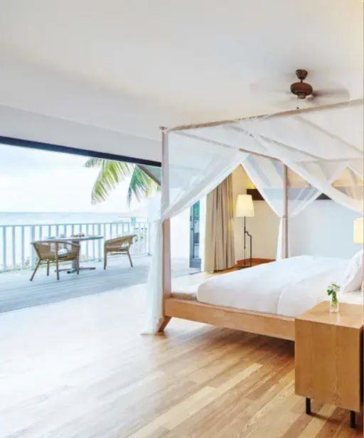 Schlafzimmer mit Blick durch geöffnete Balkontüren auf ein Holzdeck und das Meer.