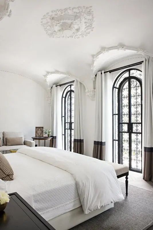 Helles Schlafzimmer mit Doppelbett, gewölbter Decke und zwei Bogenfenstern mit Gitter.