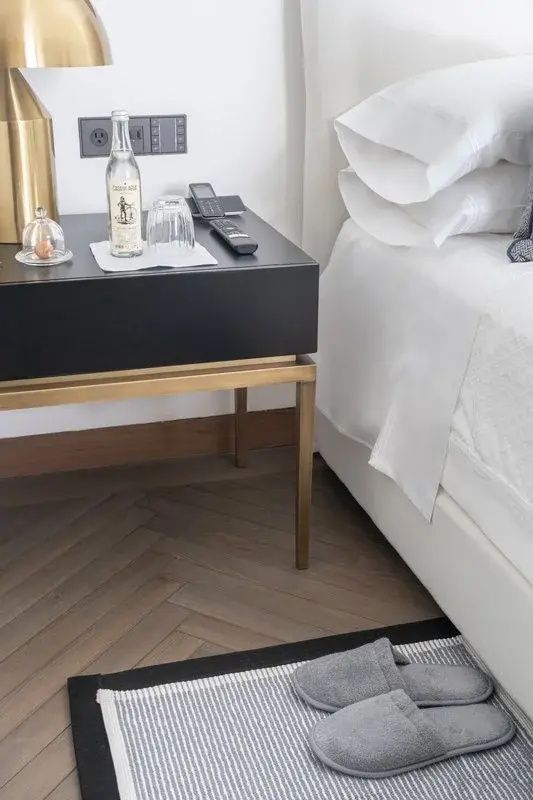 Dunkler Nachttisch mit einer Flasche Wasser und Glas neben einem Bett auf Parkett.