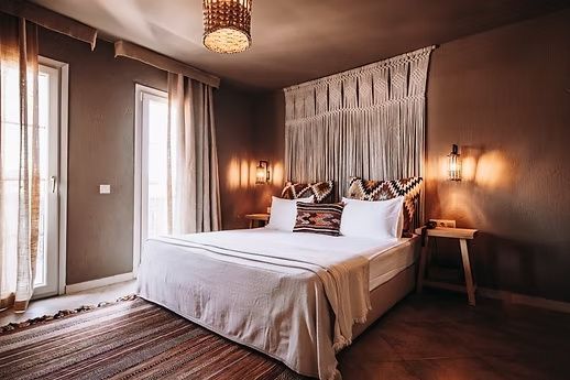 Doppelbett mit Boho-Dekoration, Makramee-Wandbehang und gemusterten Kissen im Hotelzimmer.