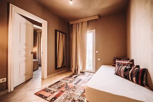 Ein helles Zimmer mit einem Schlafsofa, gemustertem Läufer, großem Wandspiegel und Vorhängen.