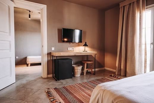 Holzschreibtisch mit Wandfernseher, kleiner Minibar und buntem Teppich im Zimmer.