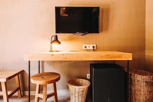 Schreibtisch aus Holz mit Fernseher an der Wand, Holzhocker und Minibar darunter.