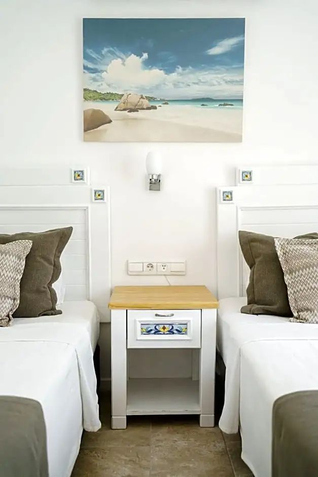 Zwei Einzelbetten mit weißen Kopfteilen, einem Nachttisch aus Holz und einem Strandbild an der Wand.