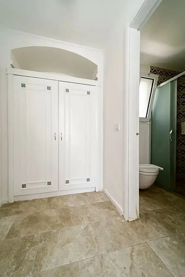 Weißer Einbauschrank im Schlafbereich und Blick in das angrenzende Badezimmer mit WC.