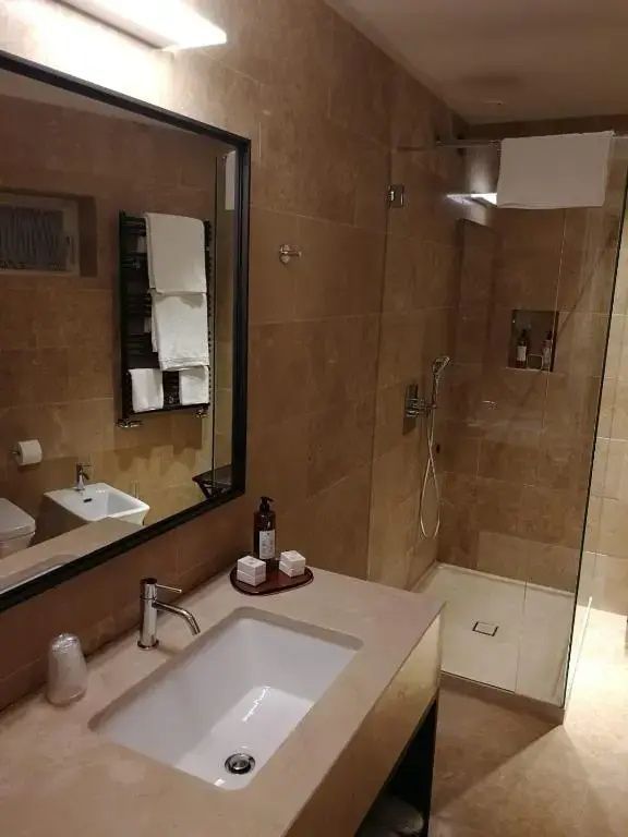 Gefliestes Badezimmer mit Waschtisch, großem Wandspiegel und bodengleicher Dusche.