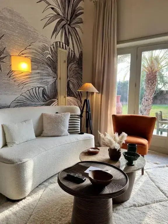 Sitzbereich mit weißem Sofa, Tischen und Blick durch das Fenster auf Palmen.