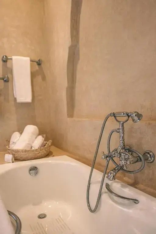 Badezimmer mit weißer Badewanne, klassischer Armatur und einem Korb mit Handtüchern.