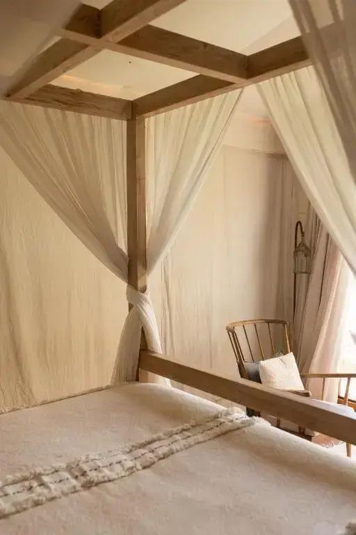 Nahaufnahme eines hölzernen Himmelbetts mit hellen Stoffbehängen im Zimmer.