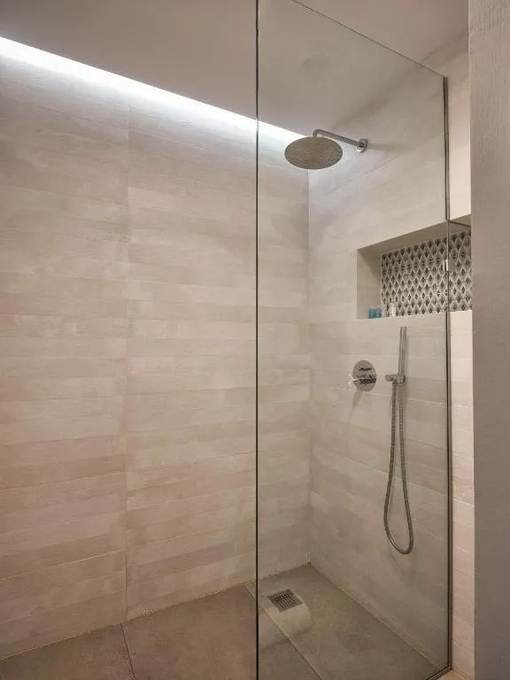 Moderne begehbare Dusche mit Regenduschkopf und hellen Fliesen an den Wänden.