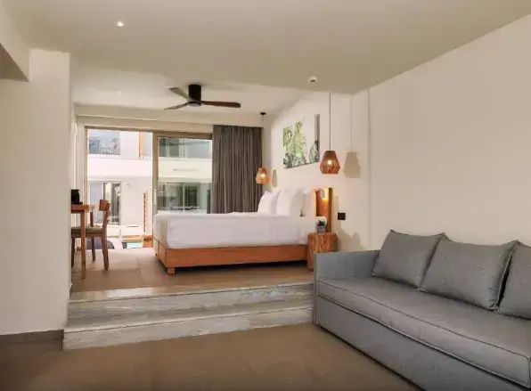 Offener Hotelwohnbereich mit einem grauen Sofa im Vordergrund und erhöhtem Doppelbett.