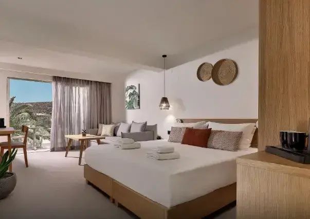 Modern eingerichtetes Hotelzimmer mit großem Doppelbett, grauem Sofa und Balkonzugang.
