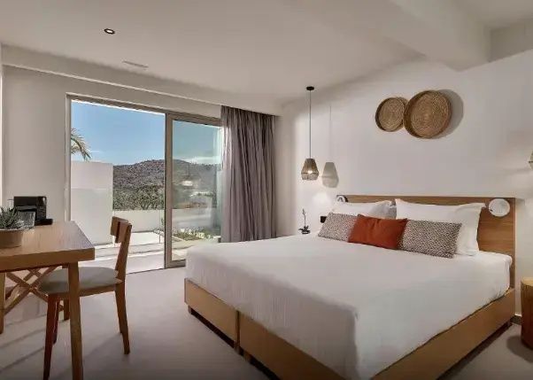Helles Schlafzimmer mit Doppelbett, Wanddekoration und großem Fenster zur Terrasse.