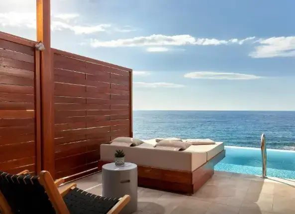 Sonnenterrasse mit einem Doppel-Loungebett, Sichtschutzwand und direktem Blick auf das blaue Meer.
