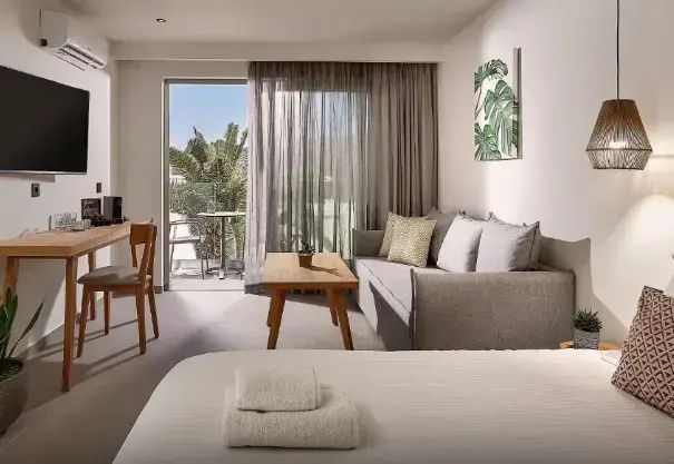 Sitzecke im Hotelzimmer mit grauem Schlafsofa, Holztisch und Blick auf den Balkon.