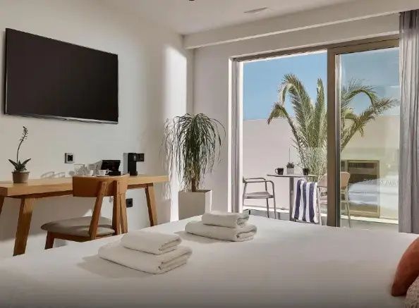 Hotelzimmer mit Blick auf Schreibtisch, Fernseher und Balkon mit Sitzgelegenheit.