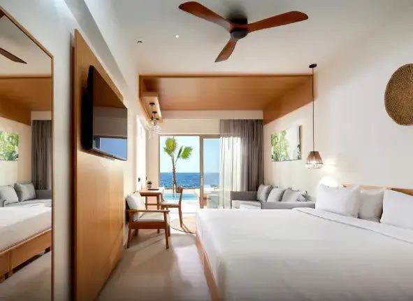 Modernes Doppelzimmer mit Fernseher, Sitzecke und Blick auf die Terrasse mit Pool und Meer.