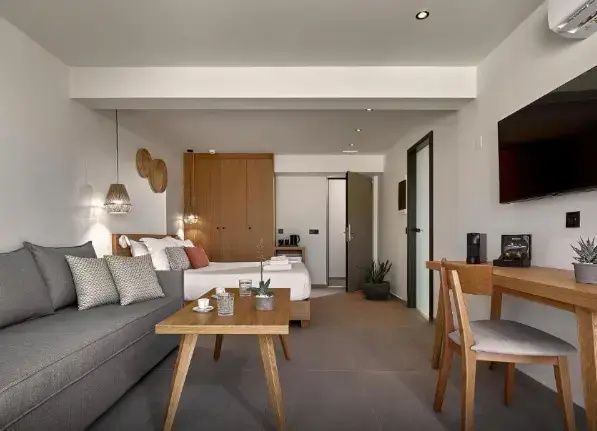 Innenansicht des Hotelzimmers mit Holzmöbeln, Holztisch, Sofa und Blick zum Eingang.