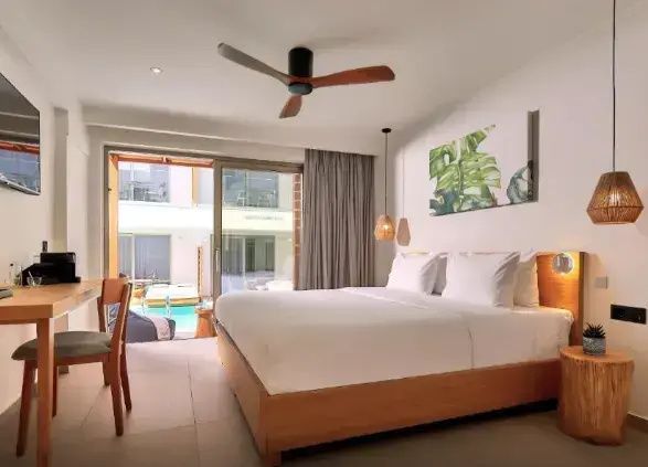 Schlafzimmer mit Doppelbett aus Holz, Ventilator an der Decke und Blick auf den Poolbereich.