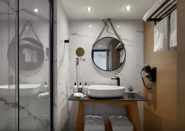 Badezimmer mit weißem Waschbecken auf einem Holzgestell und rundem Spiegel an der Wand.